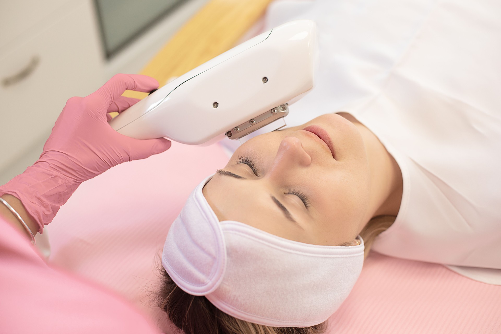 Top view of young woman lying with closed eyes, getting rejuvenation, skin-firming, deep cleaning treatment by laser.