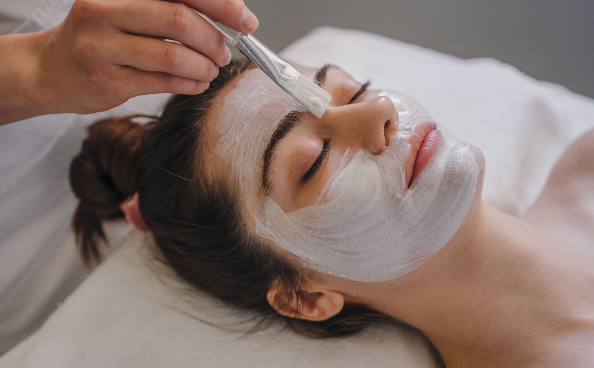 Young woman getting facial care by beautician at spa salon. Face peeling mask, spa beauty treatment, skincare. Spa concept
